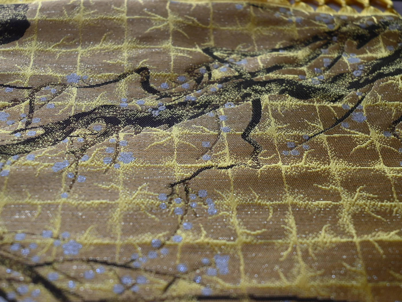 Close-up of gold Hakata-ori fabric showing dense woven texture and a branch motif